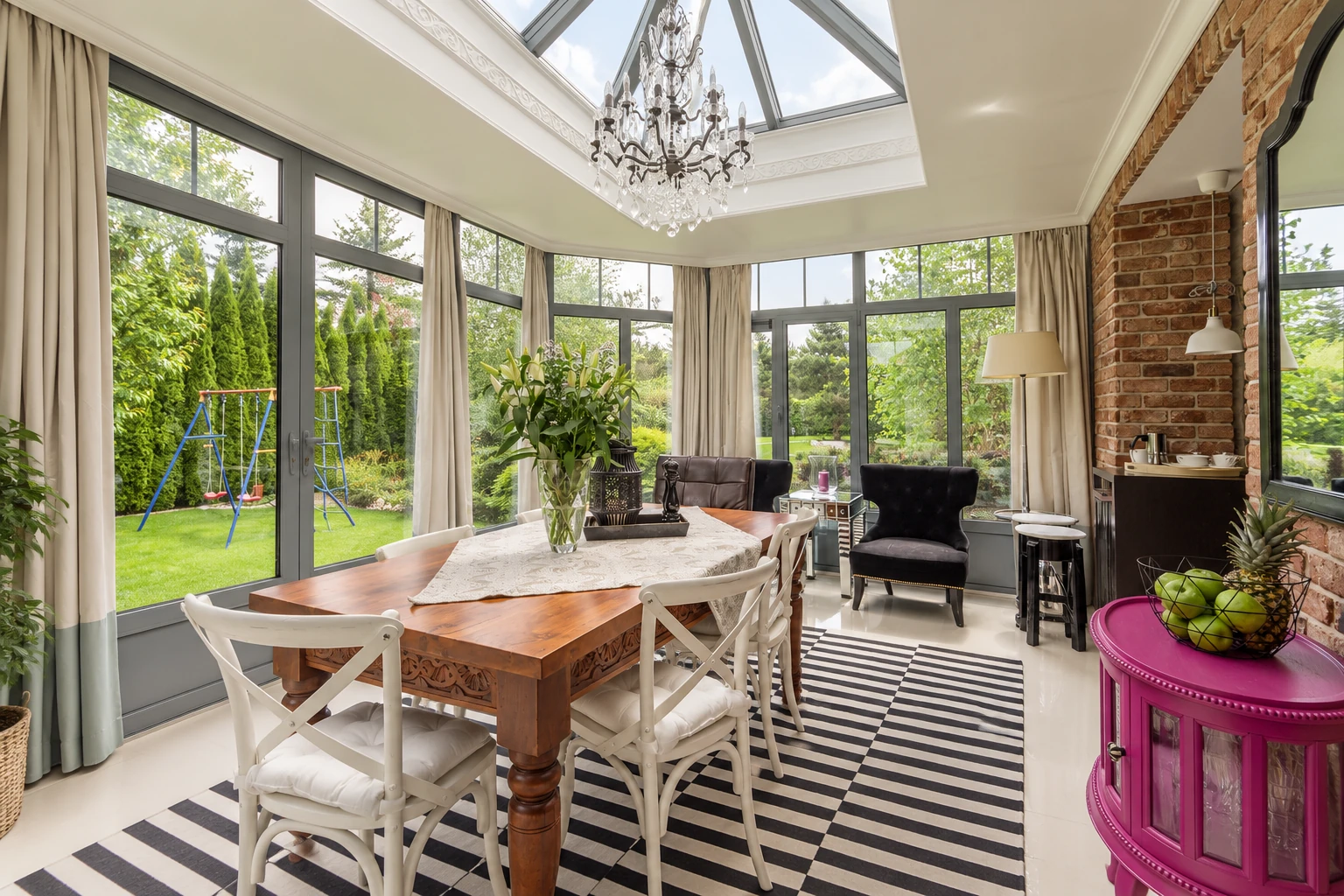 Four-season sunroom with a glass roof, large windows, dining table and chairs, and brick interior wall.