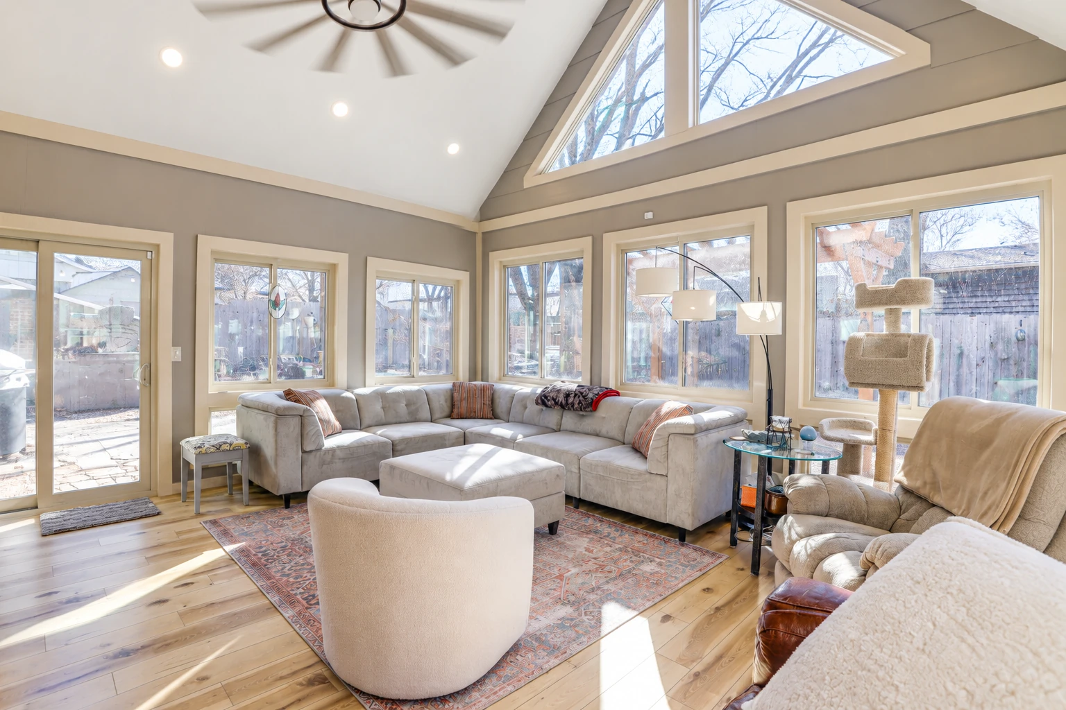 A custom sunroom with a vaulted ceiling, expansive windows, and a sectional sofa around a central ottoman.