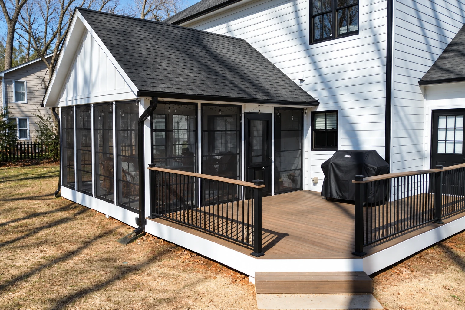 Screen room installation on a white house, with black mesh walls, a shingled roof and a wood deck.