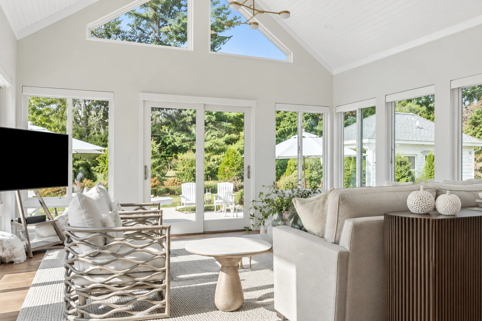 Bright white sunroom with a vaulted ceiling, expansive windows, sliding doors, and neutral seating overlooking a garden.